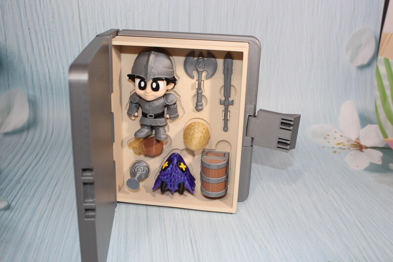 May include: A gray toy set featuring a cartoon knight figure, an axe, a sword, a barrel, and other accessories. The knight is wearing gray armor and a helmet. The set is displayed in an open gray box.