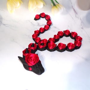 May include: A black and red rose dragon made of fabric. The dragon is curled up in a circle with its head facing the viewer. The dragon is made of black fabric with red roses attached to it.