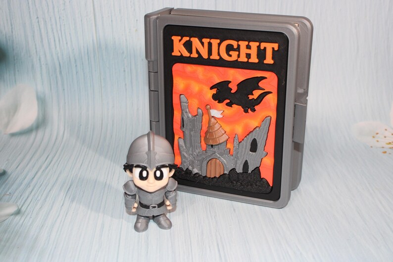 May include: A gray toy knight figure stands next to a gray case with the word "KNIGHT" in orange. The case features a castle and dragon design against an orange background. The knight figure is wearing a helmet and armor.