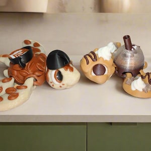 May include: Two brown and white ceramic turtle figurines with chocolate and white icing details. One turtle has a black coffee cup on its back and the other has a brown and white coffee cup on its back.