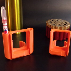May include: Two orange plastic holders for shotgun shells. The holders are empty and are sitting on a black surface.
