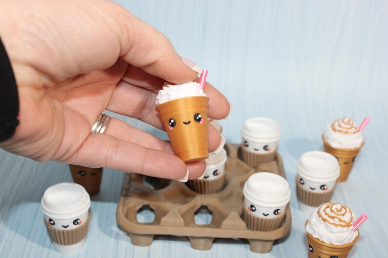 May include: A collection of miniature coffee drinks with cute, smiling faces. The drinks are in brown cups with white whipped cream and pink straws. Some are in a brown egg carton.