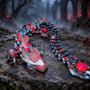 May include: A long, articulated creature figurine featuring a segmented body with a grey base, vibrant blue accents, and numerous glowing red, spherical protrusions along its back and head, resembling a multi-eyed, serpentine fantasy beast.