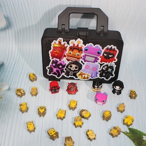 May include: A black plastic carrying case with a handle, decorated with a sticker featuring various colorful cartoon characters. Scattered in front are several small, gold-colored character figurines and a few painted miniature figures.