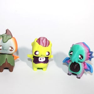 May include: Three colorful, stylized figurines. The first is orange and green, resembling a pumpkin. The second is yellow with purple accents. The third is teal, pink, and blue, with a tentacled design. All have large eyes.