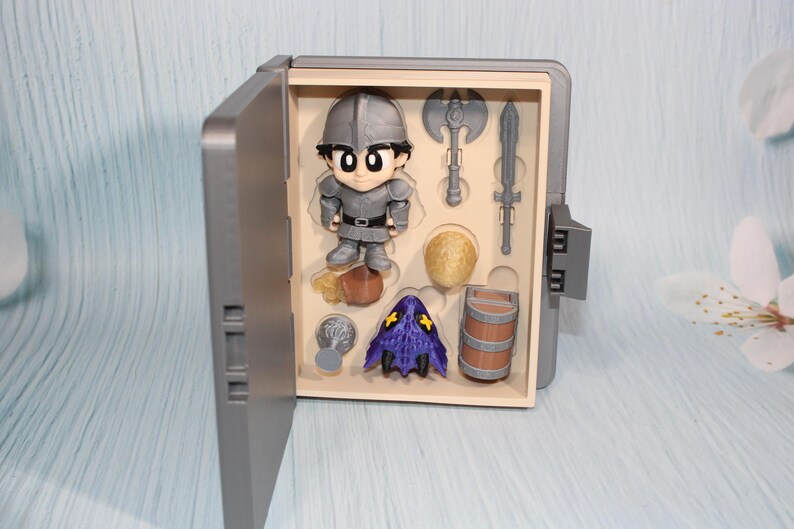 May include: A gray toy box with an open door revealing a knight figurine and miniature accessories. The accessories include a battle axe, sword, barrel, and a purple hooded figure. The knight is wearing gray armor.