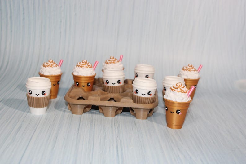 May include: An assortment of miniature coffee cups and iced coffee drinks with whipped cream and pink straws. The cups have cute, smiling faces. Some are in a brown egg carton.