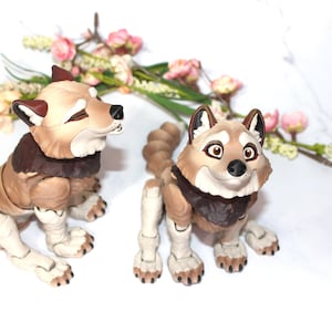 May include: Two detailed wolf figurines with tan and brown fur, dark brown accents, and white paws. One is seated, the other standing. They have expressive faces and are set against a white background with floral accents.
