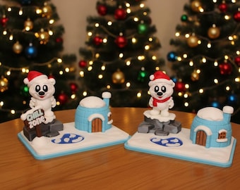 May include: Christmas-themed figurines featuring polar bears wearing Santa hats and scarves, standing next to blue igloos. One figurine holds a "Chill Zone" sign. The figurines are set on a white base with blue trim, with Christmas trees in the background.