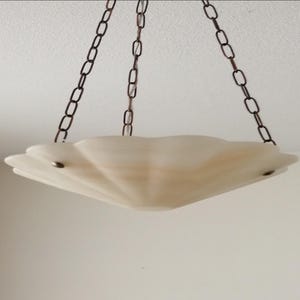 May include: A cream-colored, scalloped-edge pendant light fixture. The light hangs from three dark brown metal chains. The fixture has a shell-like design and is suspended from the ceiling. The light fixture is a decorative element.