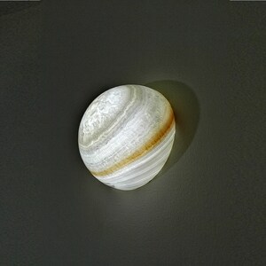 Op de afbeelding: Een witte albast bol met bruine strepen, die lijkt op een planeet. De bol wordt van binnenuit verlicht en geeft een zacht gloed.