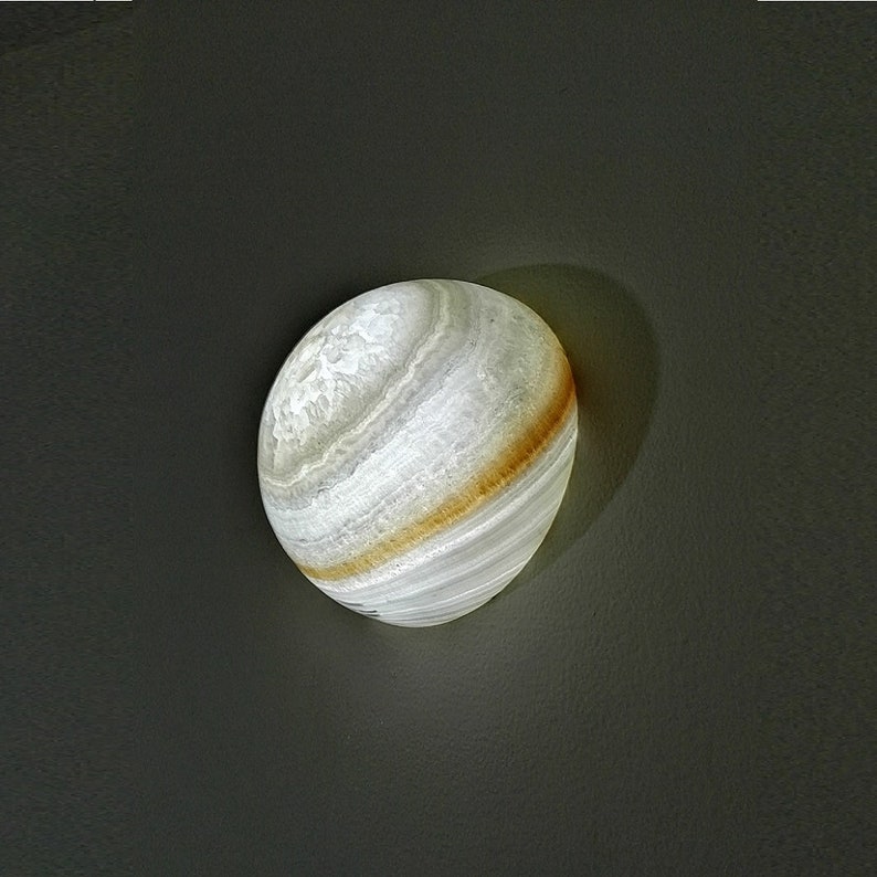 Op de afbeelding: Een witte albast bol met bruine strepen, die lijkt op een planeet. De bol wordt van binnenuit verlicht en geeft een zacht gloed.