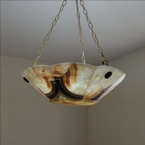 May include: A hanging light fixture with a scalloped, bowl-shaped shade. The shade is made of translucent material with brown and black veining. The fixture is suspended by gold-colored chains.