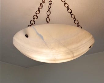 May include: A bowl-shaped pendant light fixture featuring a translucent, off-white stone shade with subtle grey veining. The shade is suspended by three dark metal chains that connect to a central mounting point at the top.