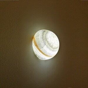 Op de afbeelding: Een ronde albasten lamp met een wit en gouden, getextureerd oppervlak.
