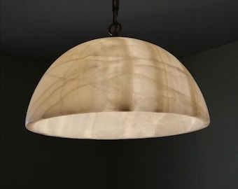 May include: A pendant light fixture with a translucent, dome-shaped shade. The shade has a marbled appearance with light and dark areas. The light hangs from a dark metal chain and is illuminated from within, casting a warm glow.