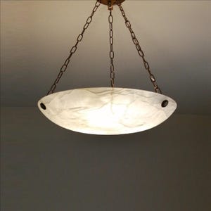 May include: A white, oval-shaped pendant light fixture with a marbled appearance. The light hangs from a bronze-colored chain and ceiling mount. The fixture has two dark holes on either end.