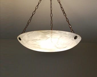 May include: A bowl-shaped pendant light fixture featuring a translucent white stone shade with natural veining. The shade is suspended by three thin metal chains connected to a central mount, with dark circular hardware securing the stone bowl.
