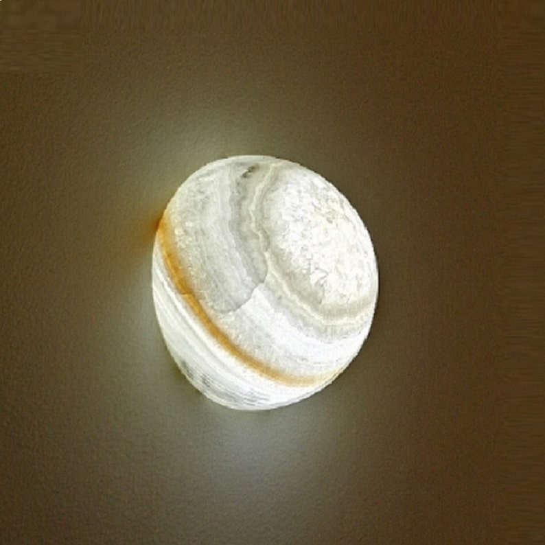 Op de afbeelding: Een ronde wandlamp van albast in wit en lichtbruin met een licht dat er doorheen schijnt.