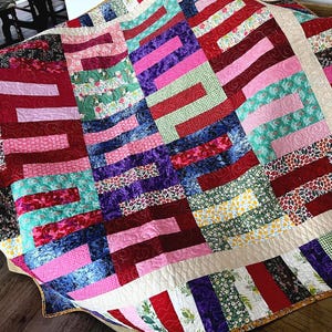 May include: A colourful quilt with a patchwork design featuring various shades of red, pink, green, blue, and purple. The quilt is made of different fabrics with floral and geometric patterns.