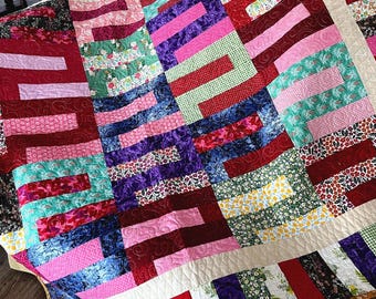 Puede incluir: Una colcha colorida con un diseño de patchwork que presenta varios tonos de rojo, rosa, verde, azul y morado. La colcha está hecha de diferentes telas con patrones florales y geométricos.