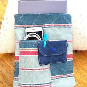 Puede incluir: Organizador de tela acolchada en tonos turquesa, gris y rojo, con múltiples bolsillos. Contiene una tableta, un smartphone y una cartera pequeña. El organizador tiene un cierre de botón.