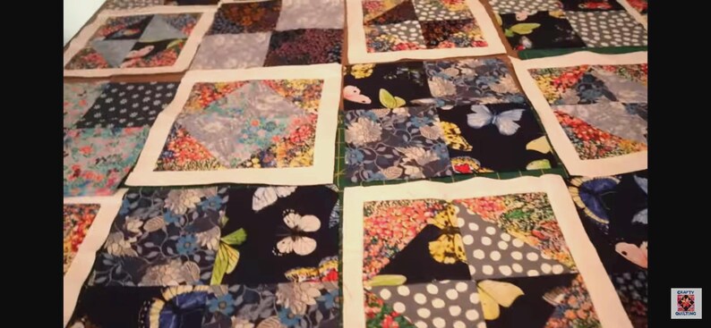 K&ouml;nnte beinhalten: Eine Decke aus verschiedenen Stoffquadraten mit unterschiedlichen Mustern, darunter Blumen, Punkte und geometrische Muster. Die Decke ist aus blauen, wei&szlig;en und gr&uuml;nen Stoffen gefertigt.