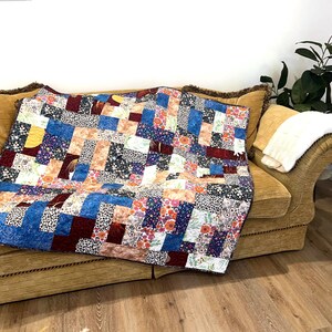 May include: A colourful patchwork quilt, featuring a mix of floral, geometric, and abstract patterns in shades of blue, red, pink, and white, is draped over a gold sofa. The quilt is made from various patterned fabrics.
