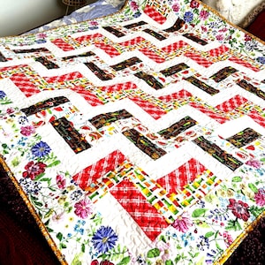 Pode incluir: Um edredom branco com um padrão chevron em tecidos vermelhos, amarelos e marrons. O edredom é enfeitado com um tecido estampado floral em tons de rosa, azul e verde.