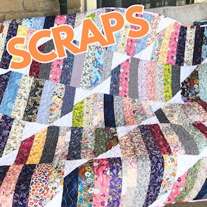 May include: A white quilt with a patchwork design made from colorful fabric scraps. The quilt is made in a chevron pattern and has the words "Scraps in a Day" printed on it.