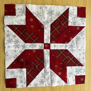 Puede incluir: Un bloque de colcha de retazos rojo y blanco con un diseño de copo de nieve. El bloque está formado por cuadrados y triángulos de tela en una variedad de patrones.