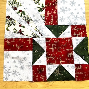 Könnte beinhalten: Ein Weihnachts-Patchworkblock in Rot, Weiß und Grün mit einem Sternmuster. Der Block zeigt ein Sternmuster mit den Worten "Hoffnung", "Licht", "Freude" und "Frieden" in goldener Schrift.