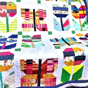 Puede incluir: Un edredón colorido hecho a mano con diseños de mariposas y tulipanes. El edredón muestra una variedad de telas estampadas en colores vibrantes como rosa, azul, verde y amarillo. El edredón está bordeado con una tela azul de lunares.