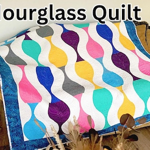 May include: A colorful quilt with a "The Hourglass Quilt" title. The quilt features a white background with a repeating pattern of hourglass-shaped designs in shades of blue, teal, pink, purple, yellow, and gray.