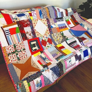 May include: A colorful patchwork quilt with a variety of fabrics and patterns, including floral, geometric, and striped designs. The quilt is made up of squares and rectangles, and it has a pink border.