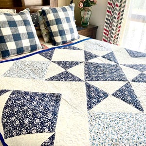 May include: A white and blue patchwork quilt with a star design. The quilt is made of different fabrics with floral patterns and a blue and white checkered pattern.