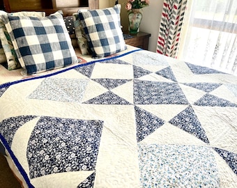 May include: A white and blue patchwork quilt with a star design. The quilt is made of different fabrics with floral patterns and a blue and white checkered pattern.