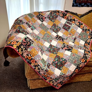 Könnte beinhalten: Eine Patchwork-Decke mit schwarzem Hintergrund und bunten Blumenmustern. Die Decke hat einen rosa Rand und liegt auf einem braunen Sofa.