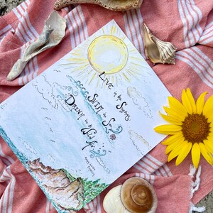 K&ouml;nnte beinhalten: Eine Aquarell-Illustration einer Sonne, Wolken und Wellen mit dem Text "Live in the Sunshine, Swim in the Sea, Drink the Wild Air." Der Text "Poppy Wilde Emerson" ist ebenfalls im Bild enthalten.