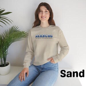 May include: A sand-colored sweatshirt with blue text that reads "Rexburg, The Land of the Frozen Chosen".