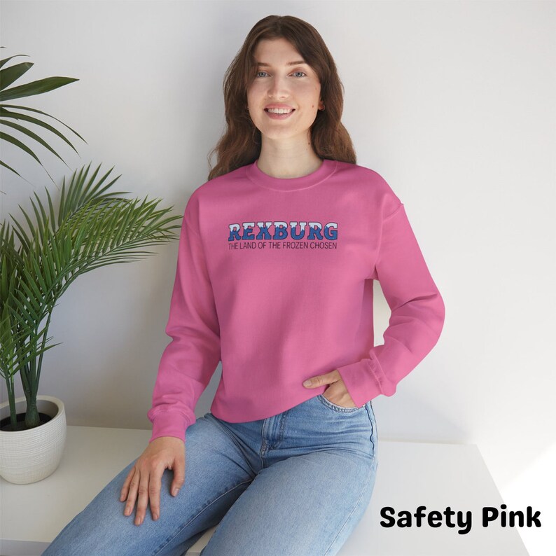 May include: A pink sweatshirt with the text "Rexburg, The Land of the Frozen Chosen" in blue and white lettering.