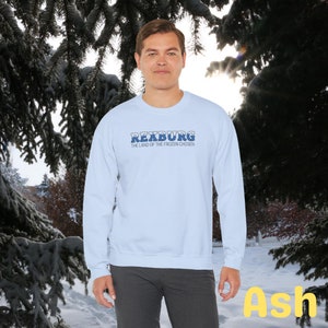May include: A light blue sweatshirt with the text "Rexburg, The Land of the Frozen Chosen" in blue lettering. The sweatshirt is being modeled by a person against a snowy background.