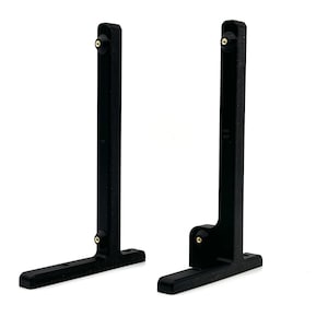 Puede incluir: Dos soportes de estante de metal negro con un diseño en forma de L. Cada soporte tiene un pequeño pomo redondo en la parte superior e inferior.