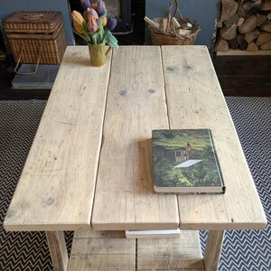 May include: A rectangular coffee table constructed from light-toned reclaimed wood planks with a lower shelf. The table surface features a book with a green forest cover and a yellow mug containing a bouquet of felted orange, purple, and blue tulips.