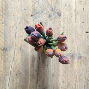 May include: A bouquet of needle-felted wool tulips in shades of deep purple, burnt orange, and muted yellow. Each flower features a rounded, closed bud shape with soft, textured petals and green felt stems bundled together in a tight cluster.
