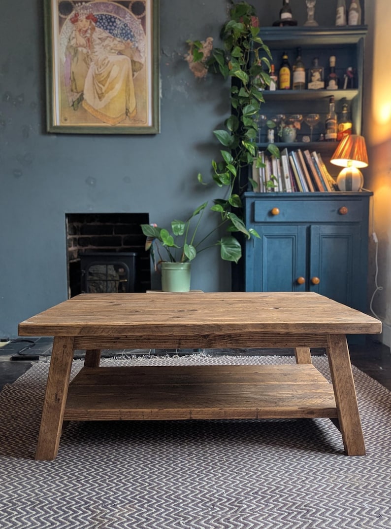 May include: A rectangular coffee table constructed from medium-brown wood with a visible grain pattern. The table features a flat top surface supported by four angled legs and includes a lower shelf positioned between the legs for additional storage.