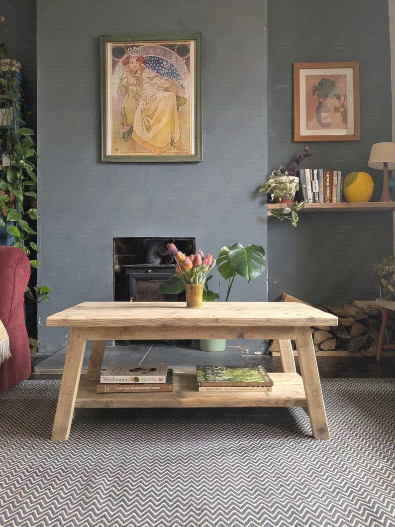 May include: A rectangular light-toned wooden coffee table with a lower shelf. The table features four angled legs and a natural wood grain finish. Two books are placed on the lower shelf, and a yellow vase with colorful tulips sits on top.