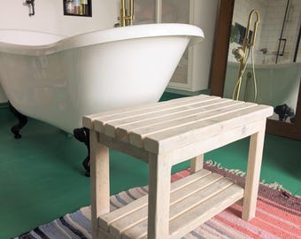 May include: A rectangular wooden bench featuring a slatted top and a lower slatted shelf. The bench is constructed from light-colored, unfinished wood with a visible grain pattern, supported by four sturdy legs in a simple, functional design.