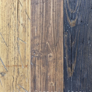 May include: Three vertical wooden planks showing distinct wood grain and texture. The left plank is light oak, the center is cognac brown, and the right is ebony black. Each plank is labeled at the bottom with the text Light Oak, Cognac, and Ebony.