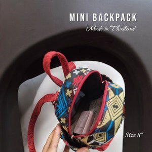 May include: A small, red, black, and gold patterned backpack with adjustable straps. The backpack is 8 inches in size and made in Thailand.  "MINI BACKPACK" and "Made in Thailand" are printed on the image.